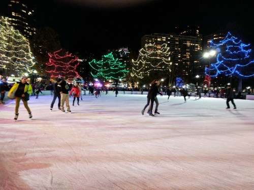 A lively ice skating rink at night, decorated with colorful lights and filled with skaters enjoying the festive atmosphere.