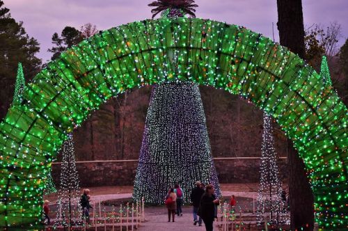 A colorful light display featuring a green arch and a tall, decorated tree, with people enjoying the festive scene.