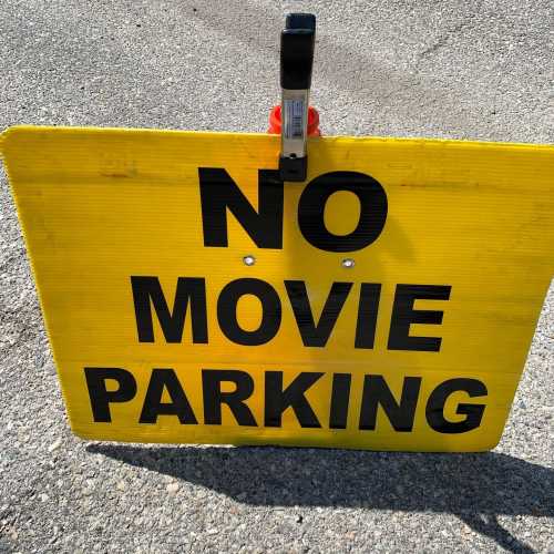 A bright yellow sign that reads "NO MOVIE PARKING" in bold black letters, placed on a gravel surface.