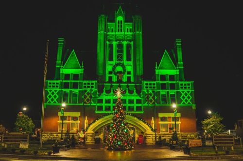 Historic building illuminated in green with a decorated Christmas tree in front, creating a festive night scene.
