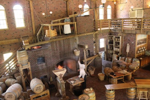A historic distillery interior with wooden barrels, a brick fireplace, and a person working in a traditional setting.