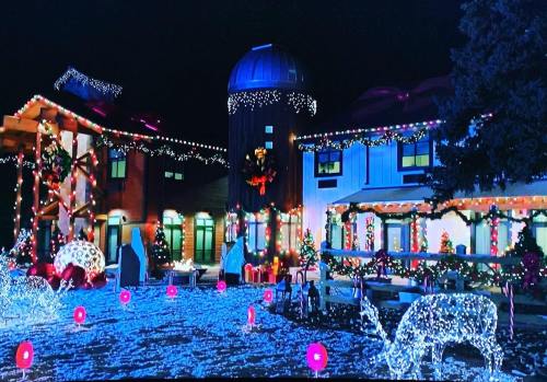 A festive scene featuring a decorated barn and house, illuminated with colorful lights and holiday decorations.