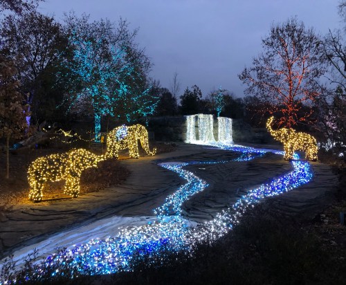 A scenic display of illuminated elephants and trees along a glowing river of lights in a twilight setting.