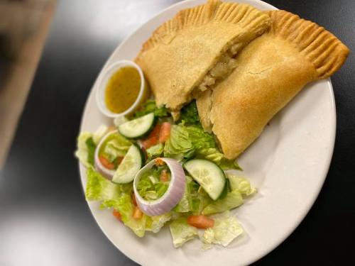 A plate with a golden-brown stuffed pastry, a side salad with cucumbers and tomatoes, and a small cup of sauce.