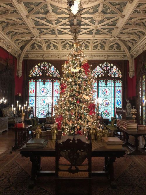 A beautifully decorated Christmas tree in an ornate room with stained glass windows and elegant furnishings.