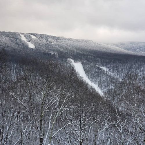 Snow-covered mountains under a cloudy sky, with ski trails visible on the slopes.
