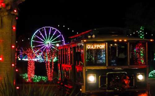 A festive trolley with colorful lights in front of a brightly lit ferris wheel at night.