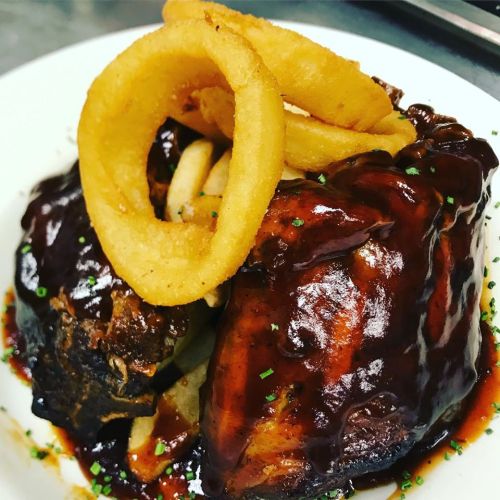 A plate of barbecue chicken with onion rings and fries, garnished with green herbs.