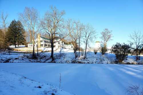 A snowy landscape featuring a white house and trees beside a frozen pond under a clear blue sky.