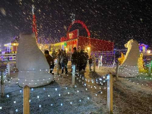 A snowy night scene with people enjoying festive lights and large chess pieces in a decorated outdoor area.