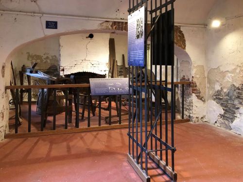 Interior of a historical building featuring a barred gate, old walls, and informational displays about the site.