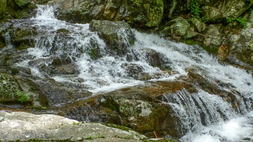 A cascading waterfall flows over rocky terrain, surrounded by lush greenery.