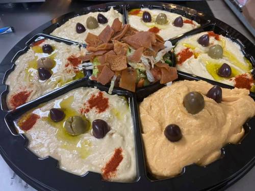 A platter of various hummus flavors, garnished with olives, spices, and crispy toppings, arranged in a circular design.
