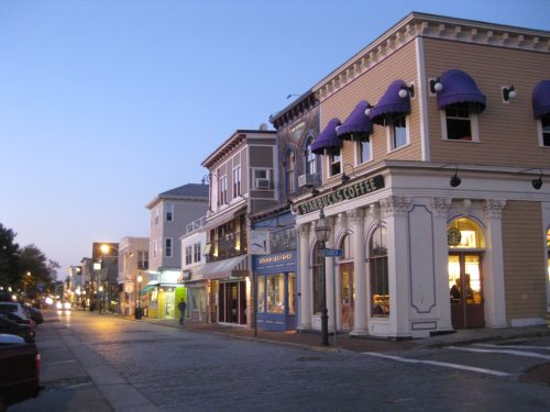 A charming street at dusk featuring shops, including a Starbucks, with purple awnings and warm lighting.
