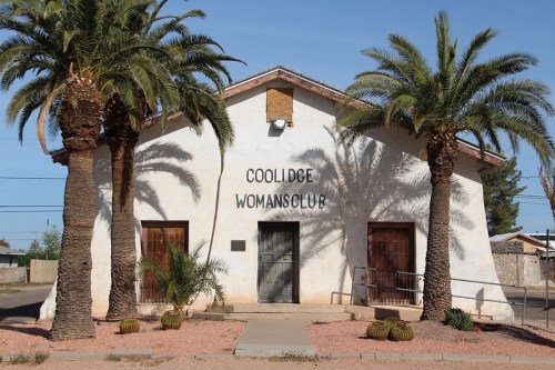 Exterior of the Coolidge Woman's Club building, featuring palm trees and a clear blue sky.
