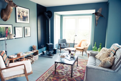 Cozy living room with blue walls, vintage furniture, a wood stove, and decorative animal mounts.