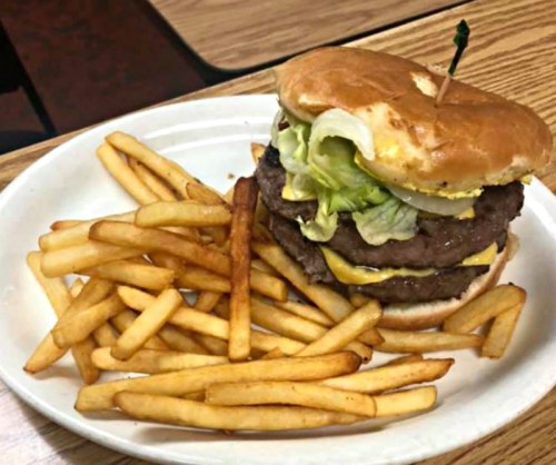 A large cheeseburger with lettuce and pickles, served with a side of golden French fries on a white plate.
