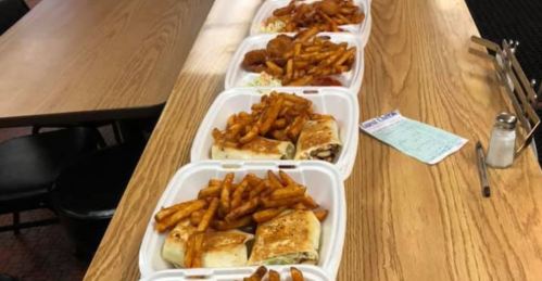 Four takeout containers on a table, each filled with fries and a wrap, alongside a small plate of coleslaw.