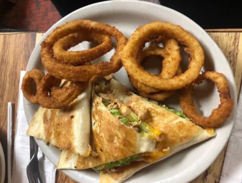 A plate with a grilled chicken quesadilla and crispy onion rings on the side.