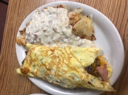 A plate with a fluffy omelet filled with vegetables and cheese, served with crispy potatoes and creamy gravy.