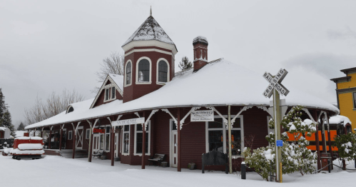 Historic train station covered in snow, featuring a distinctive tower and surrounded by a winter landscape.