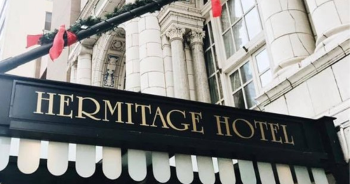 Sign for Hermitage Hotel with decorative red ribbons, featuring classic architecture in the background.