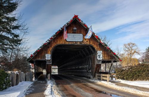 A snow-covered covered bridge adorned with flags and holiday decorations under a clear blue sky.