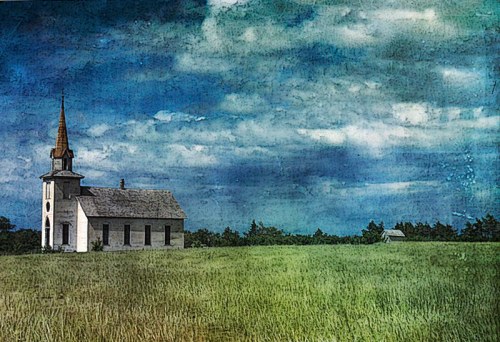 A rustic church stands in a grassy field under a cloudy sky, surrounded by trees in the distance.