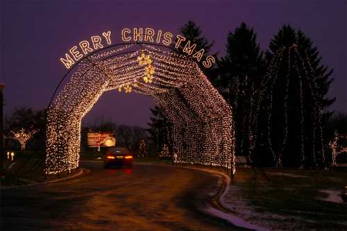 A festive archway of Christmas lights with "Merry Christmas" illuminated, set against a twilight sky.