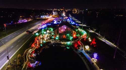 Aerial view of a festive display with colorful lights around a building and along a road at night.