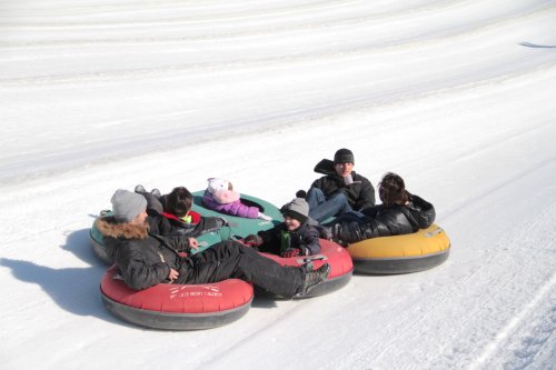 A group of children and adults sitting on colorful snow tubes on a snowy slope, enjoying a winter day.