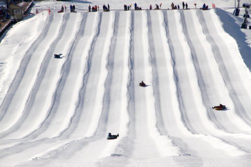 A snowy hill with multiple lanes for tubing, featuring several people sliding down on inflatable tubes.