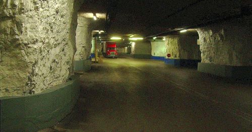 A dimly lit underground tunnel with rocky walls and a red truck parked in the distance.
