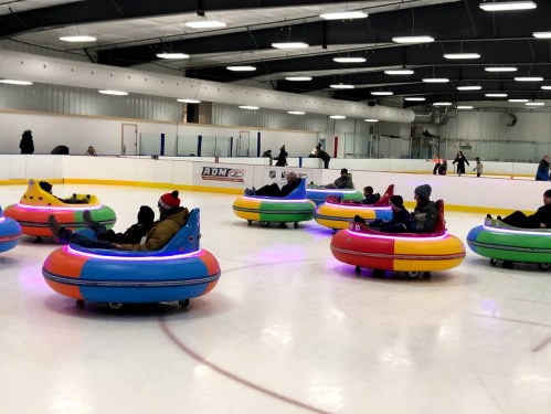 Colorful bumper cars on an ice rink, with people enjoying a fun activity in a lively indoor setting.