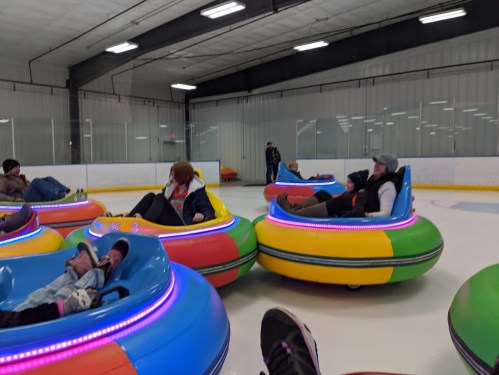 People enjoying bumper cars on ice, with colorful vehicles and a spacious indoor rink in the background.
