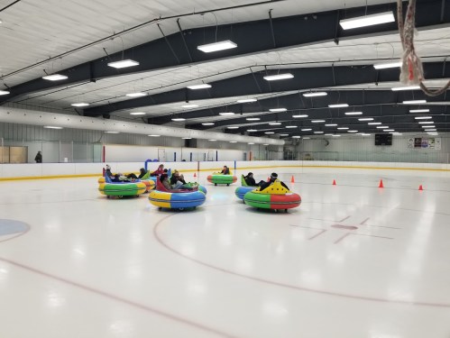 A group of people in colorful bumper cars on an ice rink, with cones set up around them.