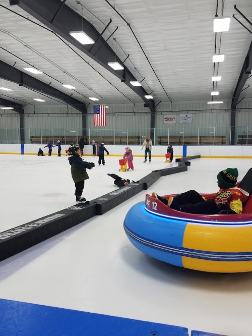 Children playing on an ice rink, some in inflatable tubes, with an American flag in the background.