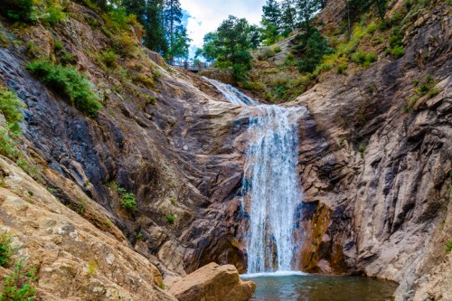 A scenic waterfall cascading down rocky cliffs, surrounded by lush greenery and trees.