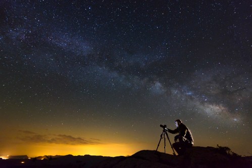 A person silhouetted against a starry sky, using a telescope to observe the Milky Way.