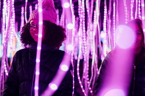 Two smiling individuals stand among vibrant purple lights, creating a festive and cheerful atmosphere.
