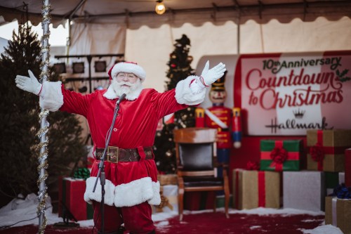 Santa Claus in a festive setting, welcoming guests with open arms at a Christmas event, surrounded by decorations and gifts.