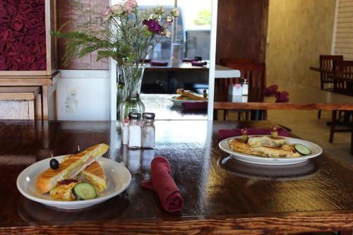Two plates of food on a wooden table in a cozy restaurant, with flowers in a vase and salt and pepper shakers nearby.