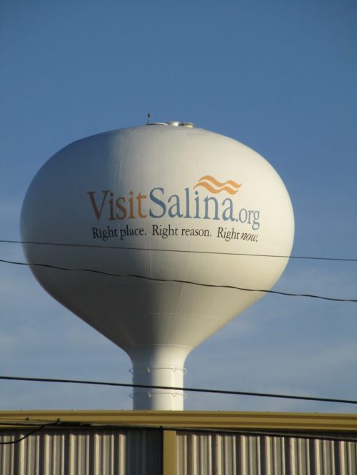 Water tower with "VisitSalina.org" and the slogan "Right place. Right reason. Right now." against a blue sky.