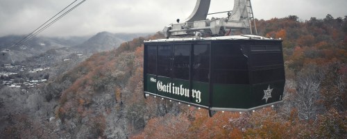 A gondola glides over autumn-colored mountains, with a scenic view of Gatlinburg below.