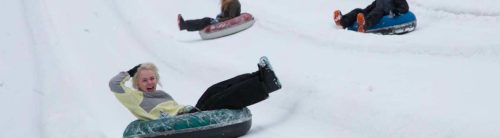 Three people sledding down a snowy hill on inflatable tubes, enjoying a winter day.