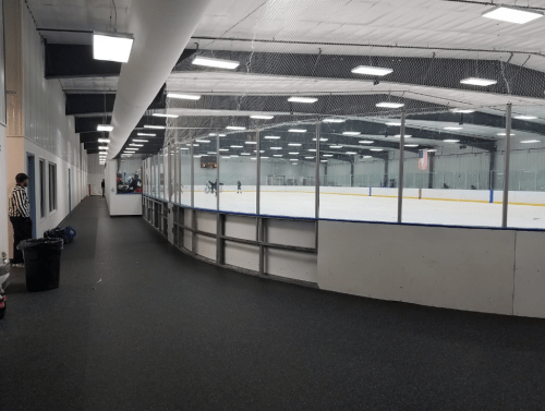 A view of an ice rink from a hallway, with a referee standing near the entrance and players on the ice.
