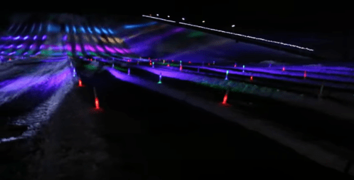Colorful lights illuminate a dark landscape, creating vibrant patterns across the ground.