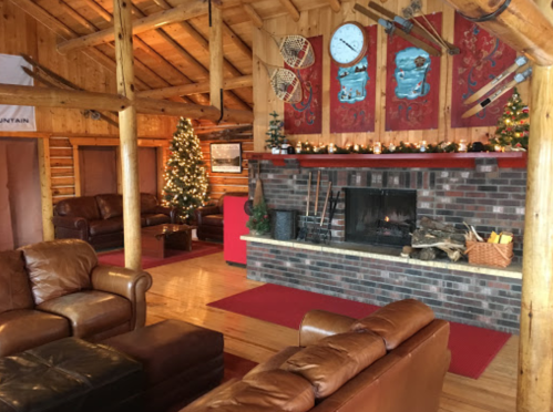 Cozy lodge interior with leather sofas, a fireplace, holiday decorations, and a Christmas tree. Warm, rustic atmosphere.