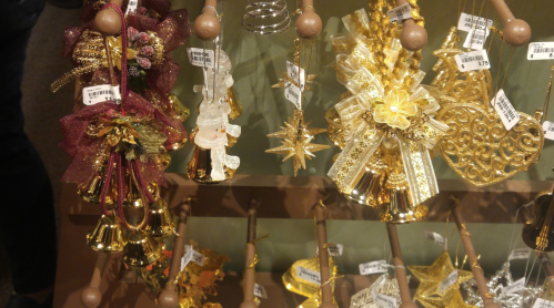 A display of decorative gold ornaments, including bells, stars, and bows, hanging on a rack with price tags.