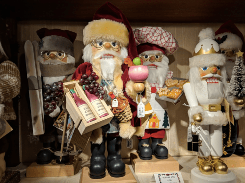 A display of festive nutcracker figurines, including Santa holding wine bottles and a drink, surrounded by holiday decor.